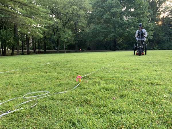 A researcher operating ground-penetrating radar equipment in a wooded field at Lookout Mountain
