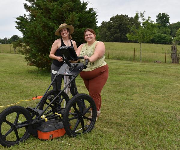 Two VISR researchers with a ground-penetrating radar cart in a field at Mud Creek Shiloh Cemetery